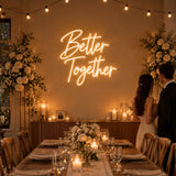 Couple at a wedding reception in front of a Better Together neon sign