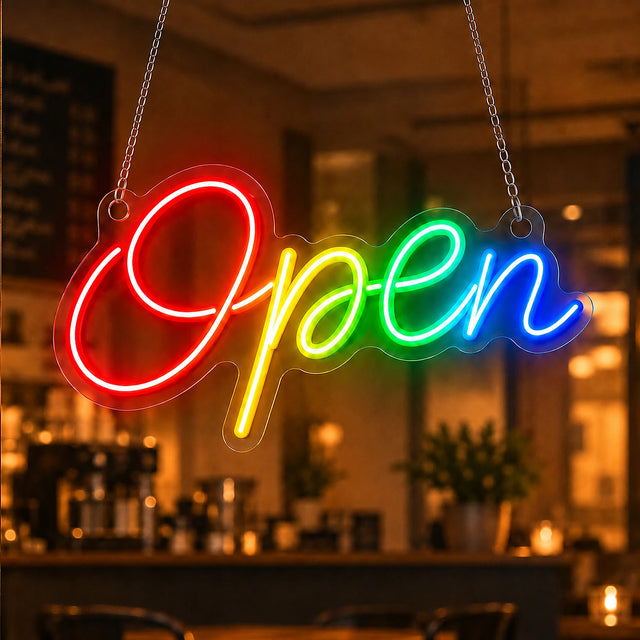 Rainbow open neon sign in script lettering glowing in a boutique window