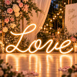 Warm white cursive Love neon sign on a floral wedding reception backdrop
