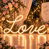 Warm white cursive Love neon sign on a floral wedding reception backdrop